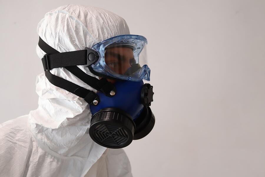 A person in a white protective suit and half-face respirator seen from the side