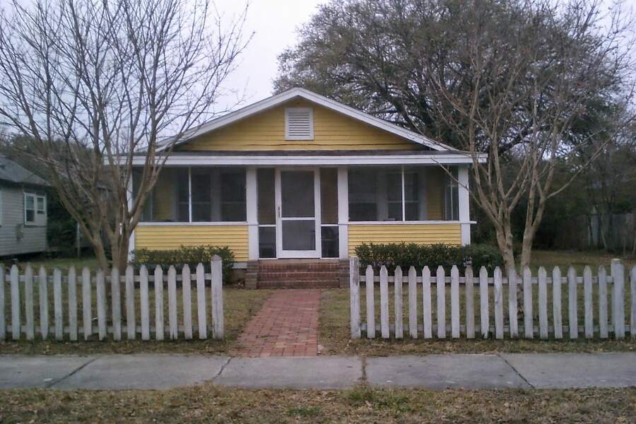 A yellow wood-frame bungalow with a front porch under bare tree limbs