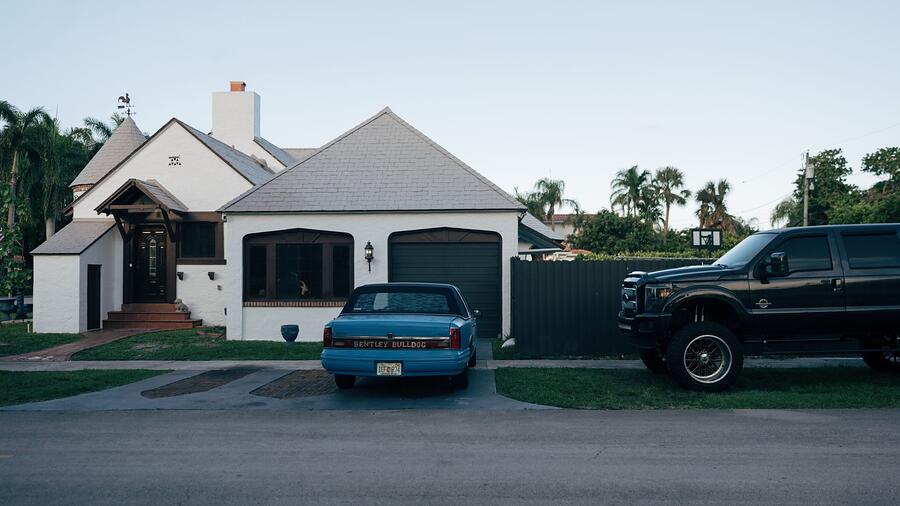 A single-story stucco house with a driveway and mature shrubs
