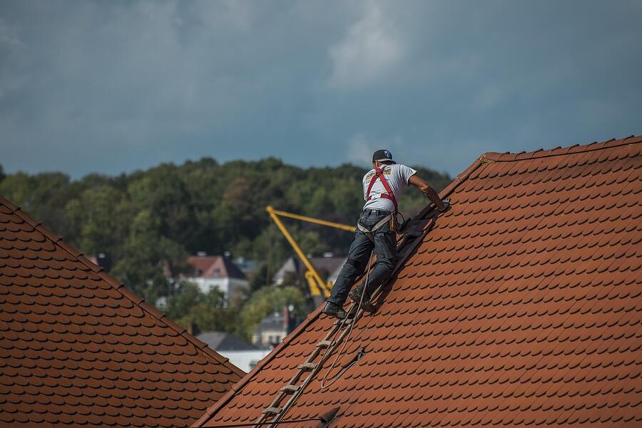 A roofer on a ladder at the eave of a barrel tile roof, seen from the ground