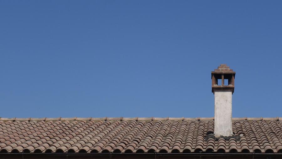 A tile roof with a chimney against a clear sky